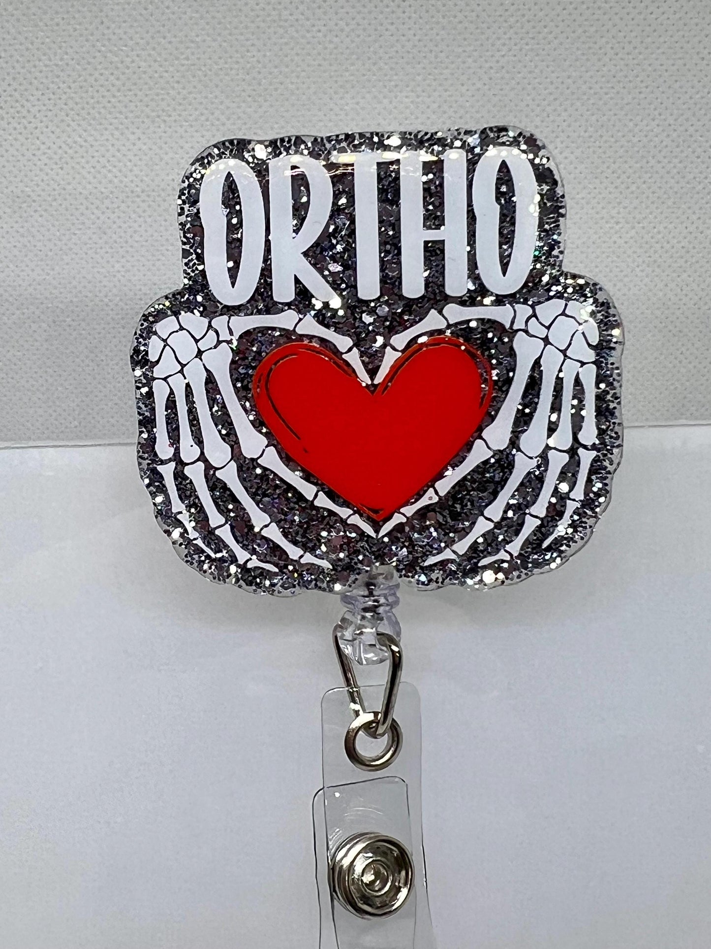 Glittery Orthopedic Badge Reel – Skeletal Hands Forming a Heart with 'ORTHO' Design, Perfect for Nurses, Doctors, and Medical Professionals