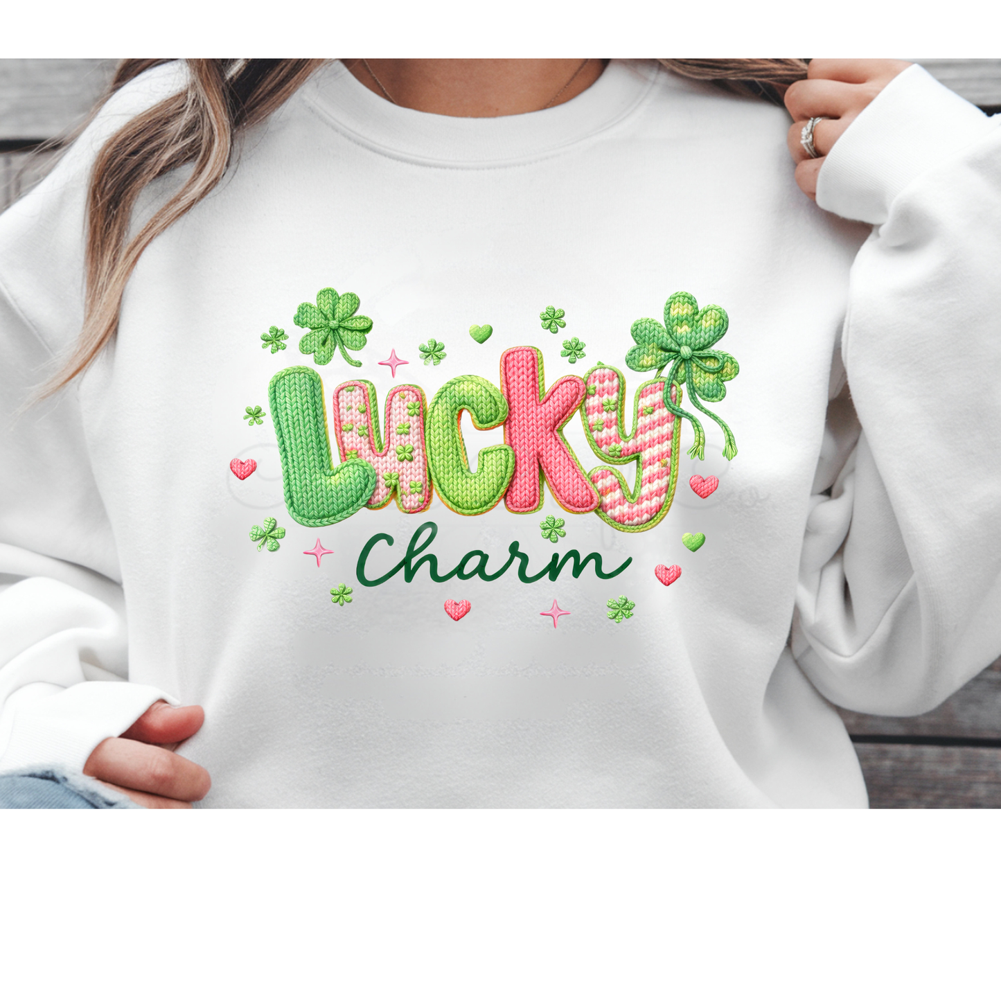 professional product mockup of a white sweatshirt featuring a St. Patrick's Day DTF transfer. The design displays the word "Lucky" in a green faux yarn embroidered texture, with the word "Charm" in pink cursive below it. A shamrock with the same yarn texture and small colorful stars surround the text.
