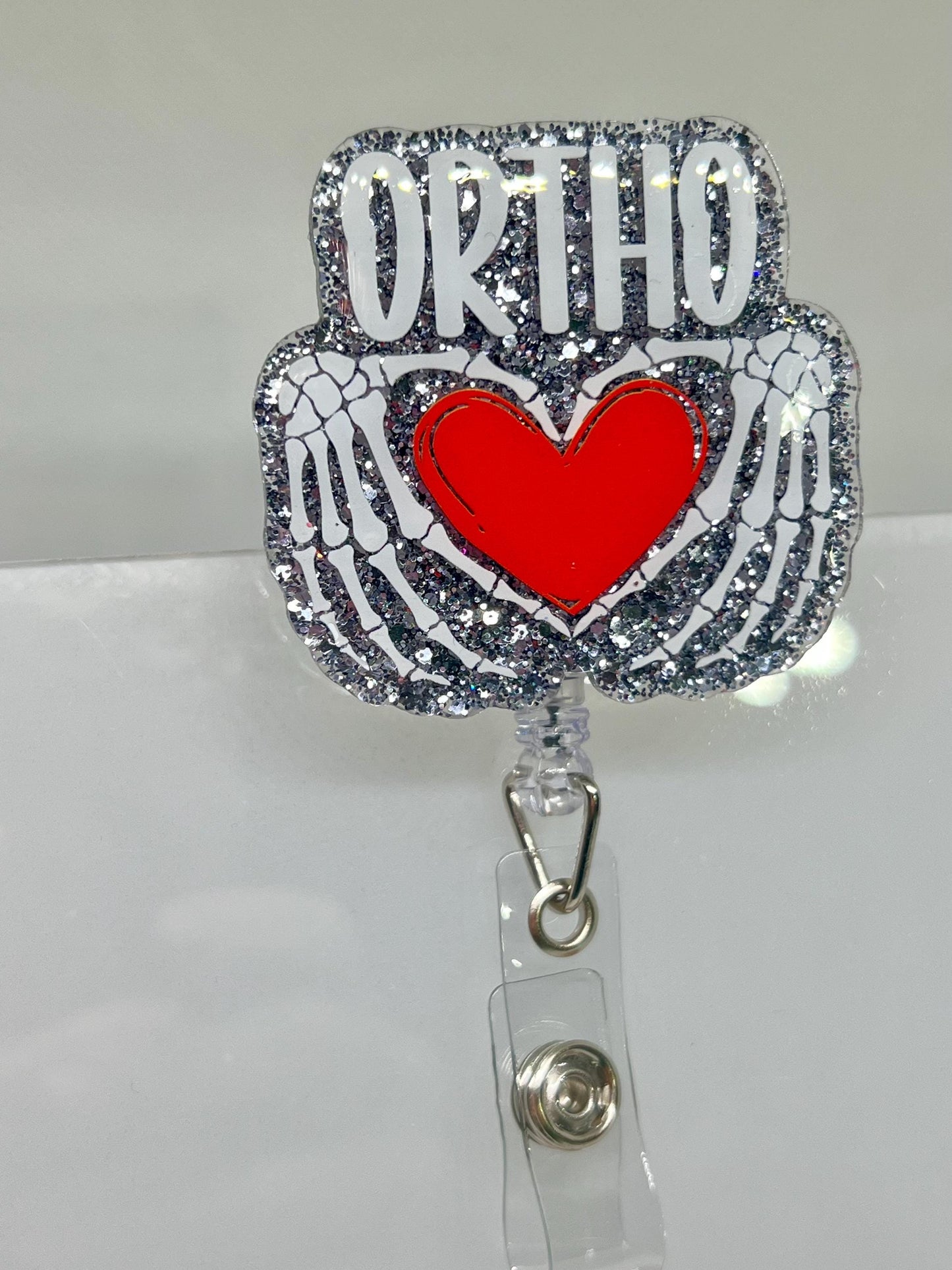 Glittery Orthopedic Badge Reel – Skeletal Hands Forming a Heart with 'ORTHO' Design, Perfect for Nurses, Doctors, and Medical Professionals