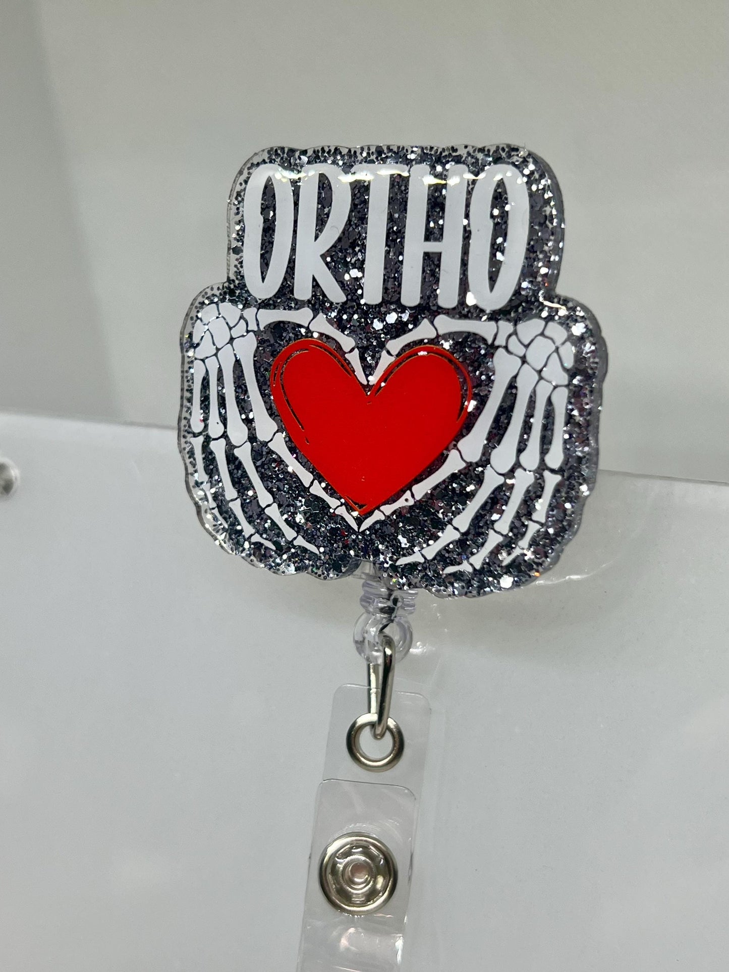 Glittery Orthopedic Badge Reel – Skeletal Hands Forming a Heart with 'ORTHO' Design, Perfect for Nurses, Doctors, and Medical Professionals