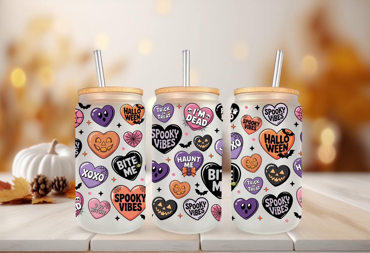 MOCKUP OF Clear glass 16oz can tumbler with a bamboo lid and glass straw, decorated with a pastel Halloween conversation hearts UVDTF wrap featuring phrases like Spooky Babe and Bite Me, displayed alongside iced drinks and fall decorations.