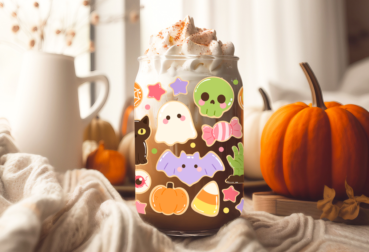MOCKUP OF Clear frosted glass 16oz can tumblers with bamboo lids and glass straws, decorated with a pastel Halloween sugar cookies UVDTF wrap featuring ghost cookies, mummy cookies, candy corn, and skull lollipops.