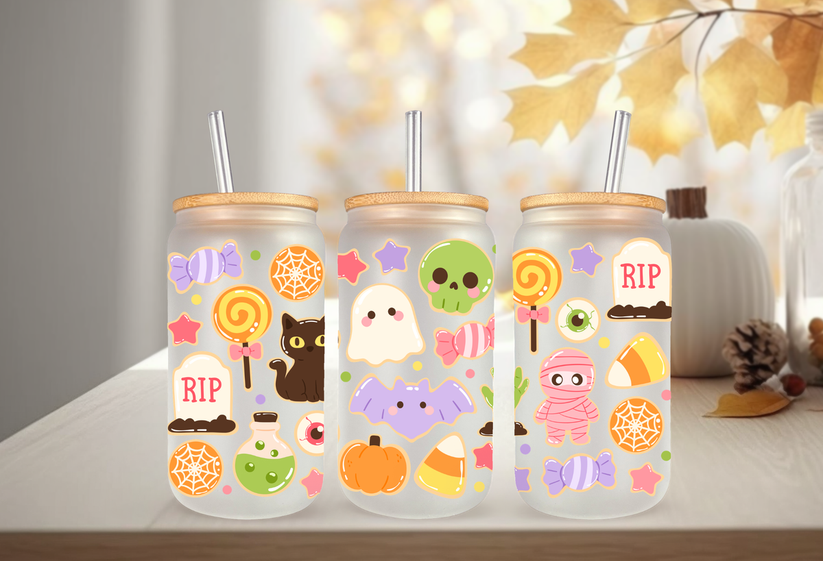 MOCKUP OF Clear frosted glass 16oz can tumblers with bamboo lids and glass straws, decorated with a pastel Halloween sugar cookies UVDTF wrap featuring ghost cookies, mummy cookies, candy corn, and skull lollipops.