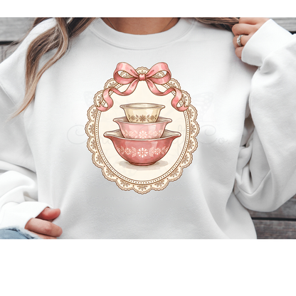 Direct to Film (DTF) transfer design featuring a vintage stack of blue and white nesting mixing bowls topped with a pink coquette bow and framed by a white lace border