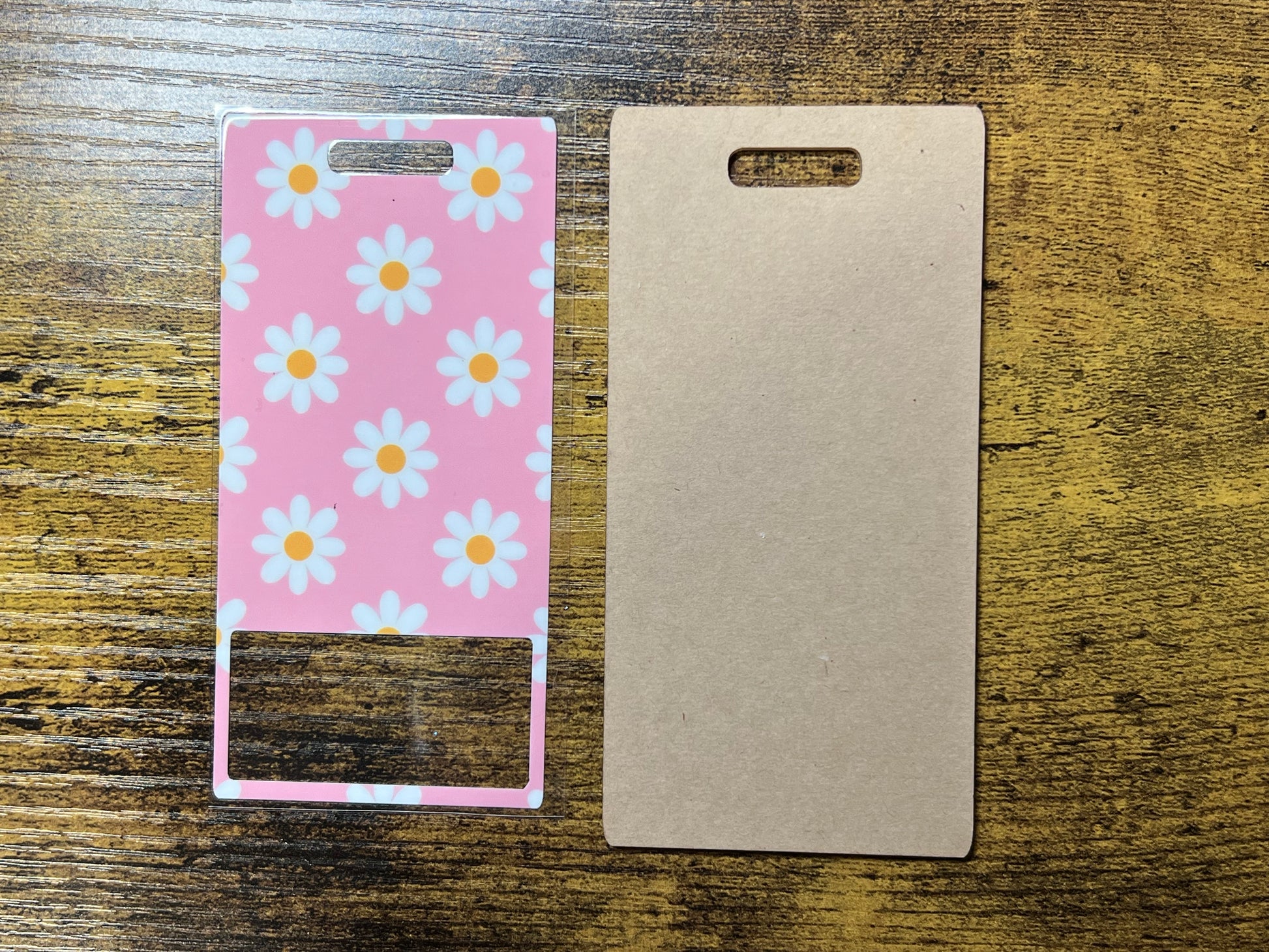 two items placed on a wooden surface: a pink card with white flowers and a blank card.