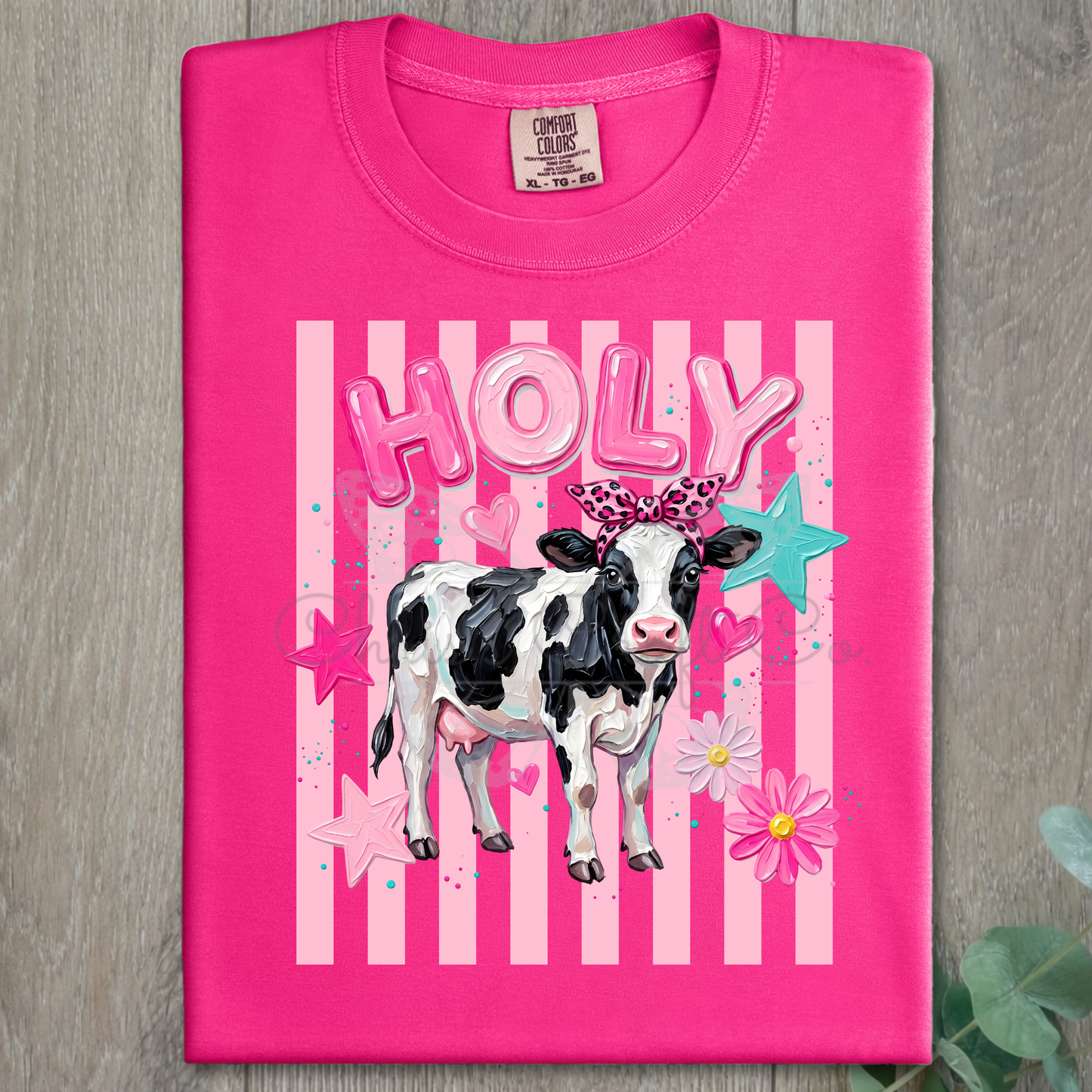 MOCK UP OF A Ready to press DTF apparel transfer on a hot pink t-shirt featuring a black-and-white country cow with a pink leopard bow, pink bubble letters, and a turquoise star backdrop.