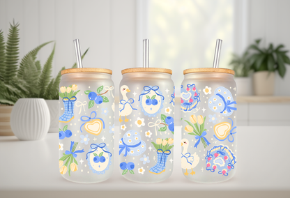 16oz can glass wrap featuring a pastel spring design with white porch geese wearing blue coquette bows mixed with yellow tulips and scattered blueberries.

