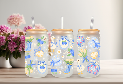 16oz can glass wrap featuring a pastel spring design with white porch geese wearing blue coquette bows mixed with yellow tulips and scattered blueberries.

