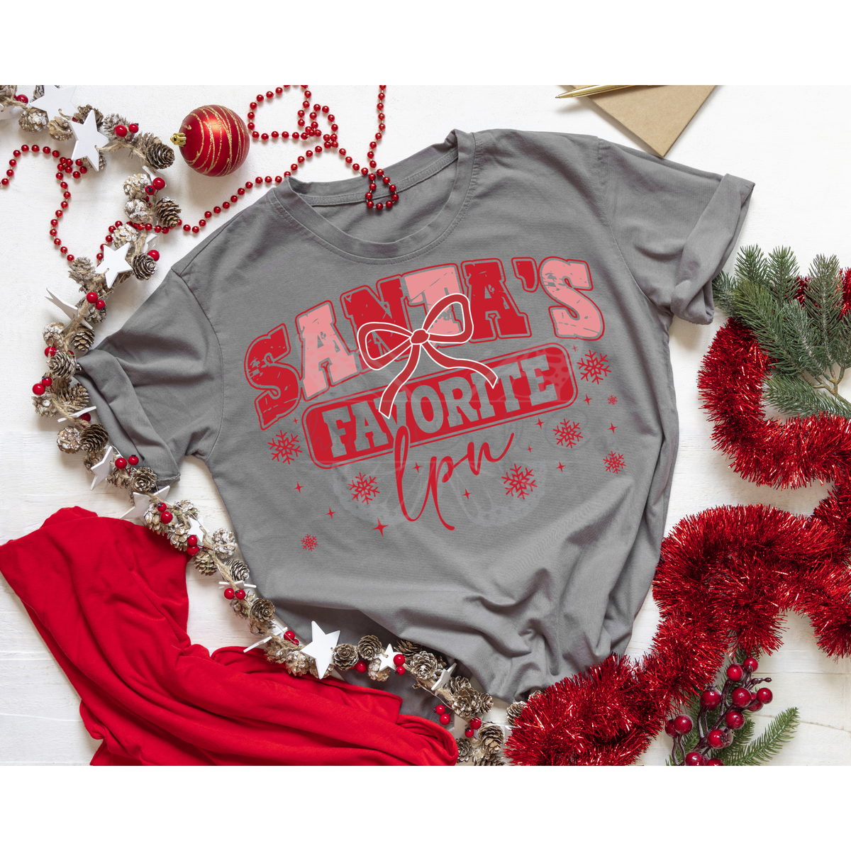 Grey t-shirt mockup featuring a Santa's Favorite LPN DTF transfer with red and pink glitter text and snowflakes.
