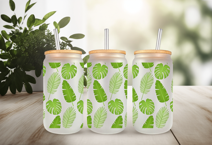 mockup of a 16oz frosted can glass wrap featuring a vibrant green botanical design with detailed monstera leaves and tropical palm fronds on a clear background.