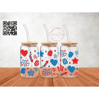 Three glass cups with patriotic-themed decorations, featuring stars and stripes in red, white, and blue colors, displayed on a wooden surface 