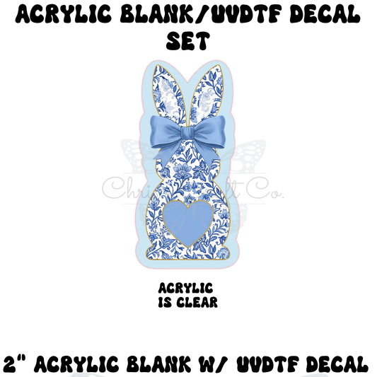 A DIY badge reel kit featuring a clear bunny-shaped acrylic blank and a UV DTF decal with a blue and white floral chinoiserie pattern, a blue bow, and a blue heart.