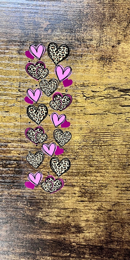 A UV DTF pen wrap transfer featuring a vertical row of hearts with alternating designs of solid purple and leopard print patterns, shown with a 3D glossy finish on white pens.